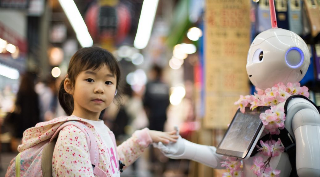 Japanisches Mädchen schüttelt einem Roboter die Hand.