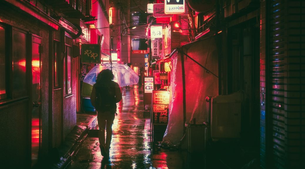Person mit Regenschirm geht durch eine neonbeleuchtete und regnerische Gasse in Japan.