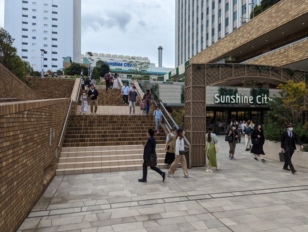 Das Einkaufszentrum "Sunshine City" in Ikebukuro von außen mit Treppen die zu einer kleinen Grünanlage führen.