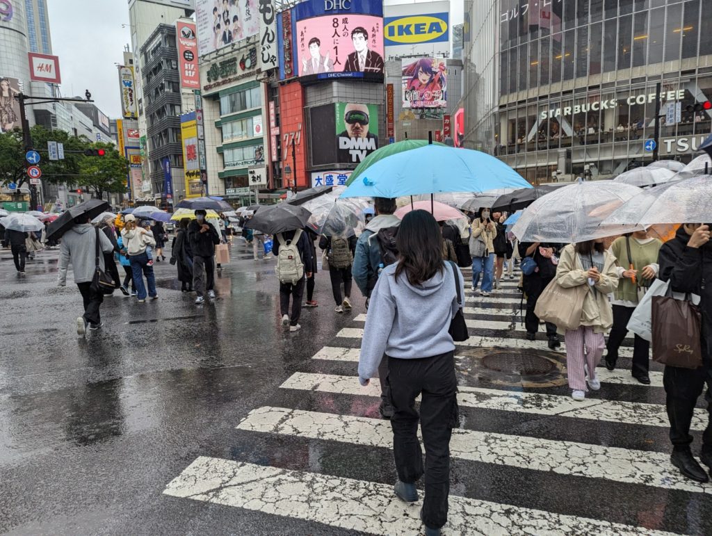 Die große Kreuzung in Shibuya bei Regen. Fast alle Personen tragen Regenschirme.