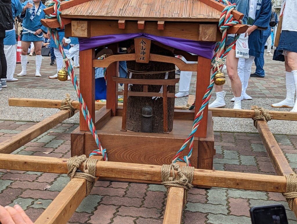 Ein Mikoshi, ein tragbarer Schrein der einen hölzernen Phallus beherbergt, sowie einen weiteren kleinen vor einem Torii-Tor