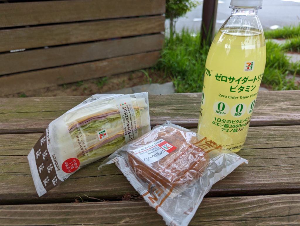 Sandwich, Currybrötchen und ein Getränk aus dem 7-Eleven auf einer Parkbank.