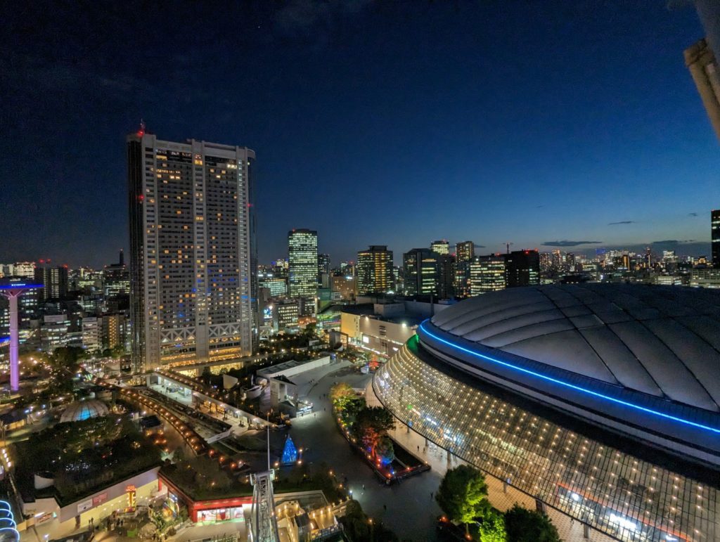 Der Blick vom hohen Riesenrad auf das nächtliche Tokio. Ein Meer von Lichtern. Man sieht auch das Stadion Tokyo Dome.