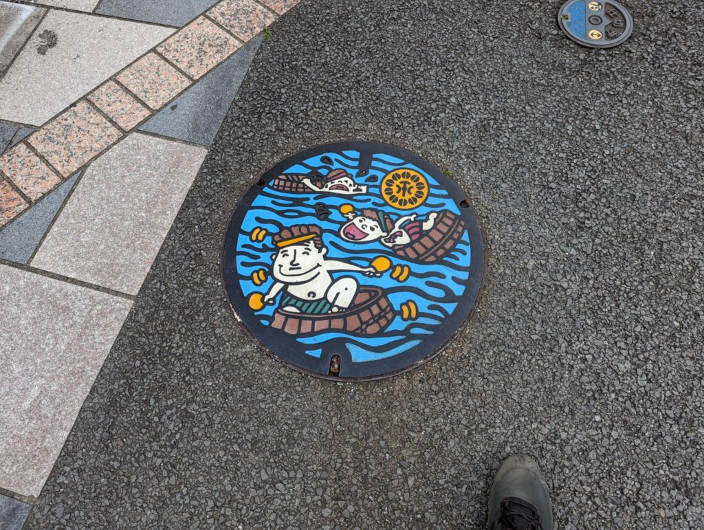 Ein Gullideckel der eine Familie zeigt, die in Wasserbottichen paddeln.