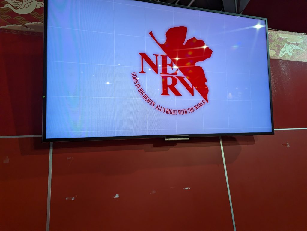 Ein Monitor zeigt das NERV-Logo aus dem Anime Neon Genesis Evangelion.