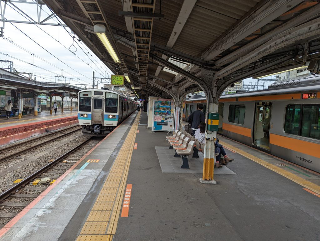 Ein Bahnhof in Tokio, an dem zwei unterschiedliche Linien an benachbarten Gleisen stehen.