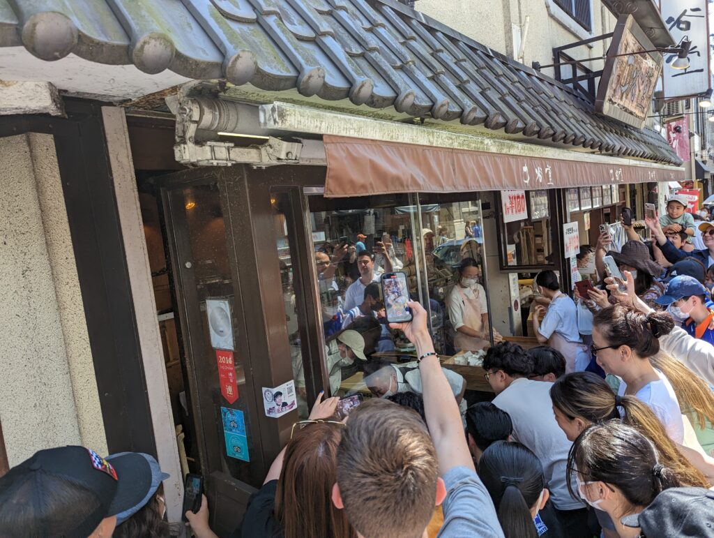 Ein Mochi-Stand in Nara um den sehr viele Menschen stehen, größtenteils mit Smartphones filmend.