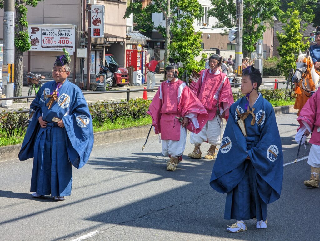 Mehrere kostümierte Festteilnehmer gehen in einer Parade eine Straße entlang.