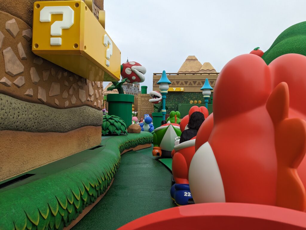 Eine Fahrt in der Attraktion "Yoshis Adventure" in der Nintendo World. Der Wagen fährt an den ikonischen Fragezeichen-Boxen der Mario-Spiele vorbei.