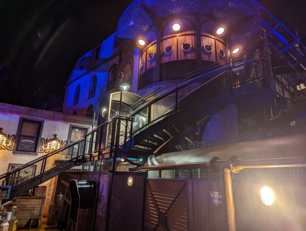 Die Steampunk-Welt Rookburgh im Phantasialand, mit Blick auf das Hotel Charles Lindbergh bei Nacht. Die Belecuchtung einiger Ele,ente ist blau.
